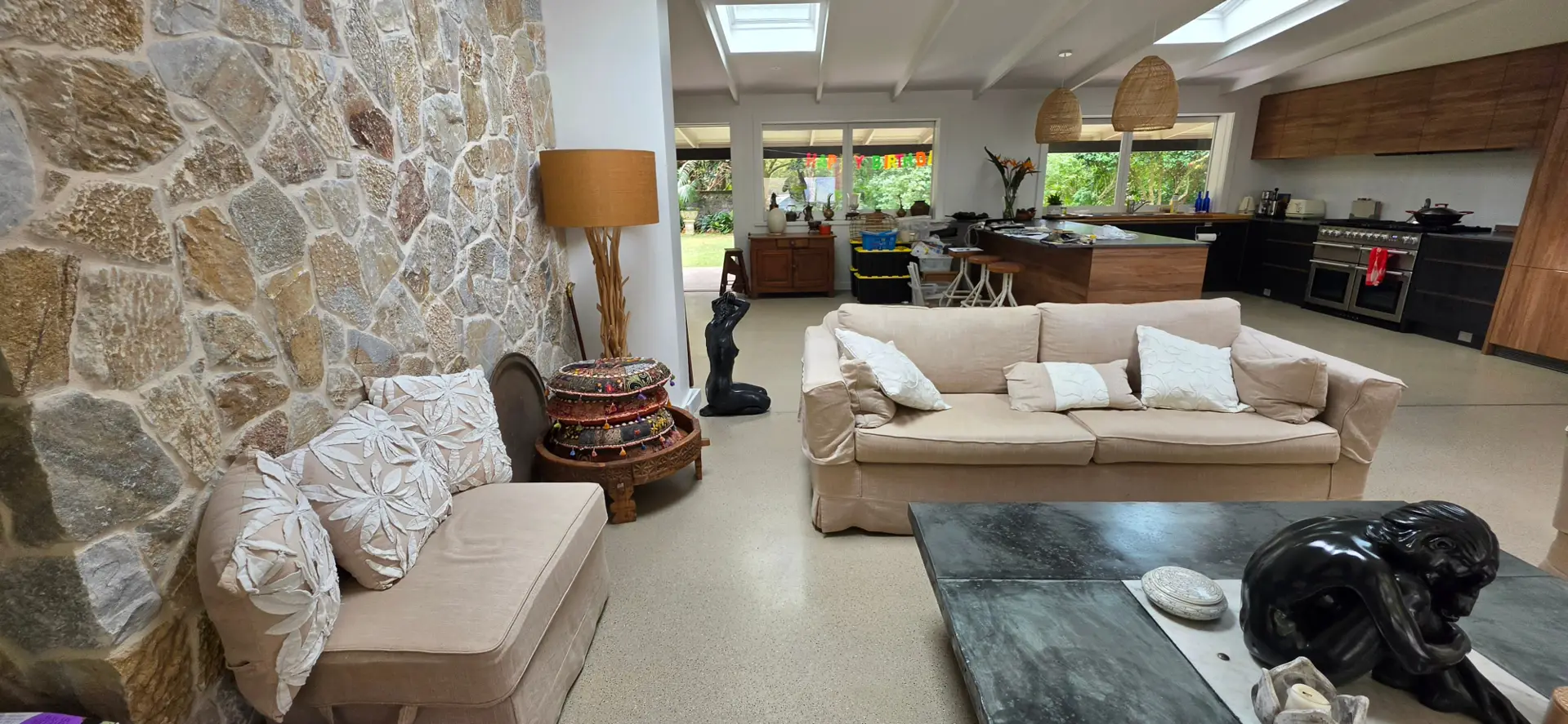 A polished concrete floor running through the open-plan living and kitchen area of an Avalon Beach home, with a stone feature wall and garden views beyond