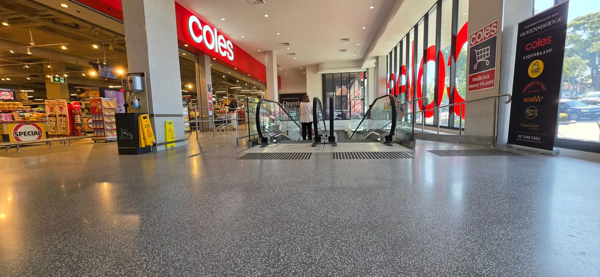 Polished terrazzo floor across the entrance concourse at Coles Caringbah, looking toward the escalators