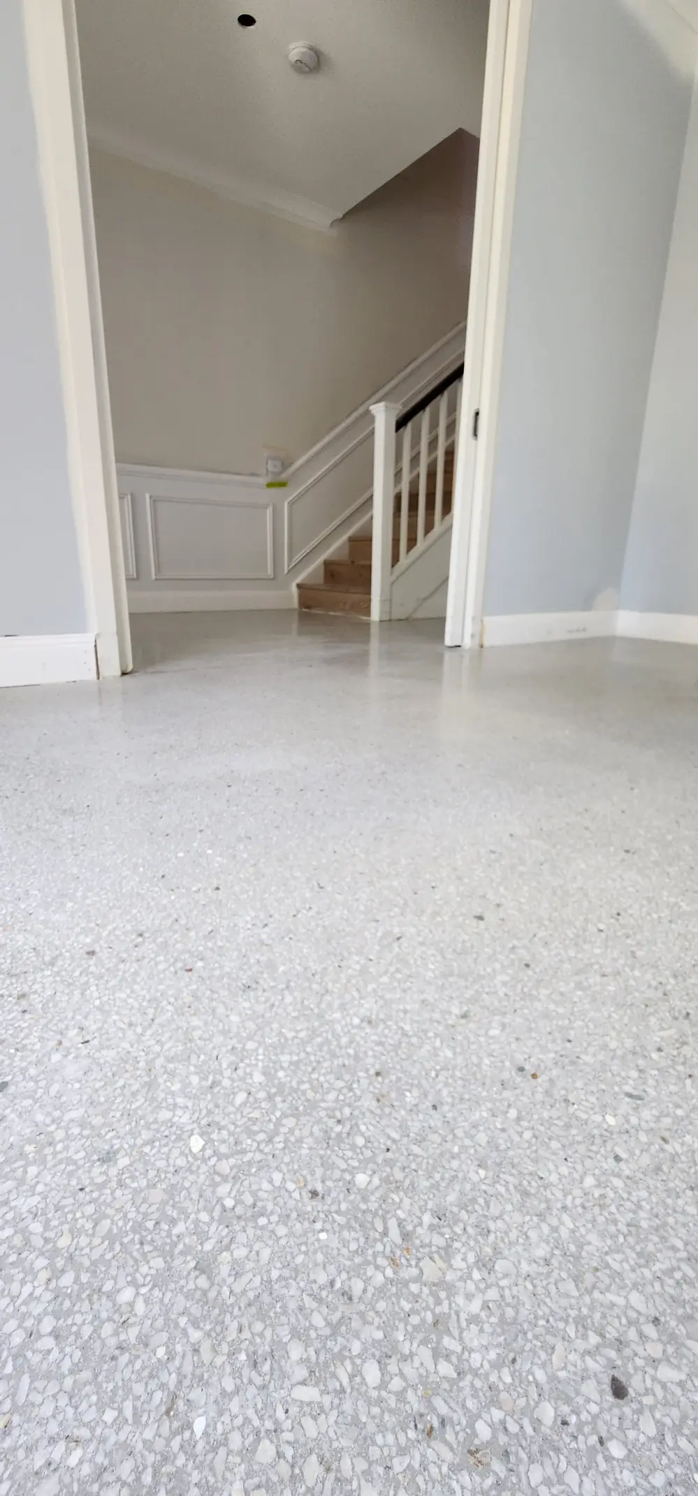 A pale polished terrazzo floor with large white and grey marble aggregate running through an entry hall toward a staircase