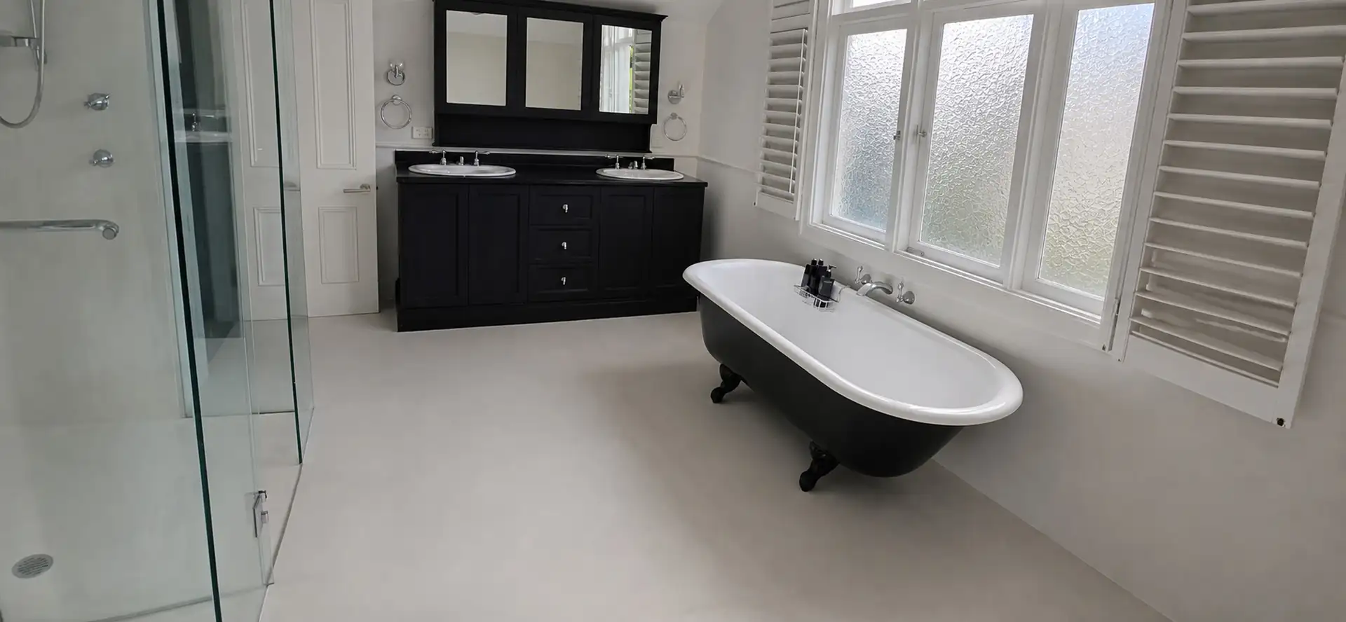 Manly ensuite after — seamless microcement floor with a freestanding bath and dark vanity