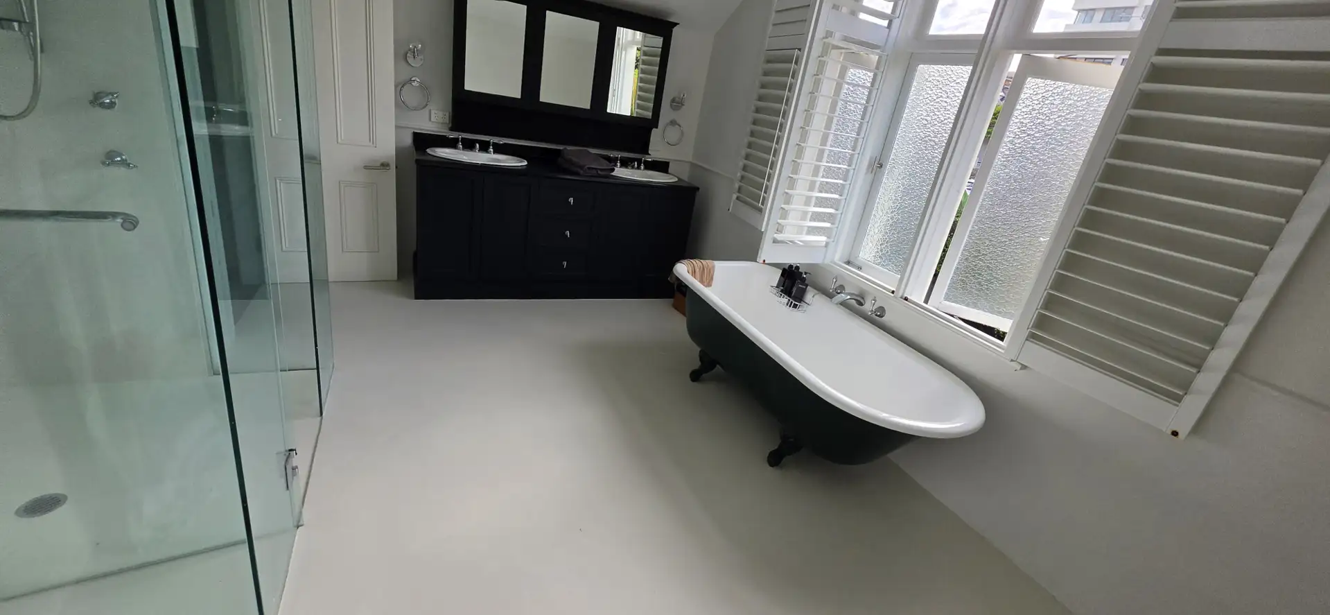 Manly ensuite after — seamless microcement floor with a freestanding bath and dark vanity