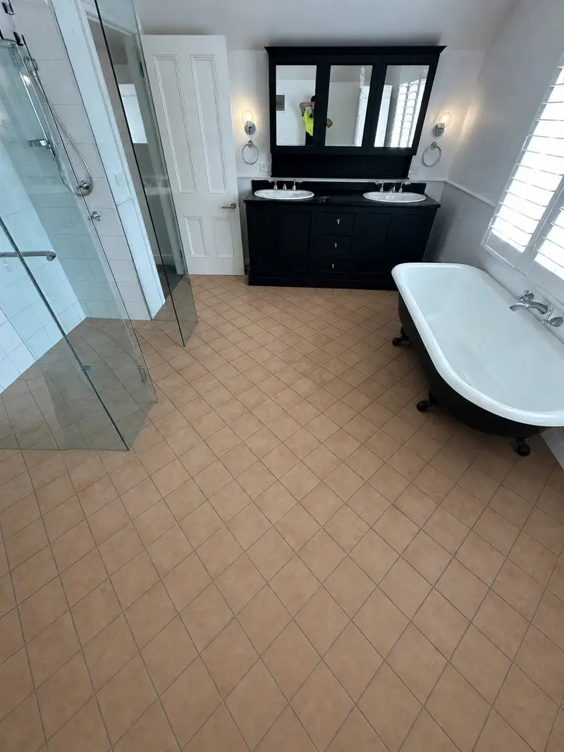 Manly bathroom before — a dated tiled floor with grout lines, kept in place